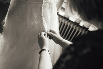 Close up on bridesmaid's hands fastening wedding dress buttons. Bridesmaid helping bride to dress....