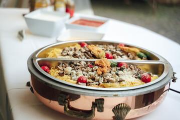 Food warmer with 2 portions of pasta, champignons, cheese and tomatoes. Self-service buffet table. Celebration, party, birthday or wedding concept.