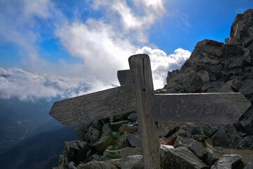 青い空、白い雲、北アルプスの奥穂高岳のわかれみちに立つ木製の道しるべ。西穂高岳、前穂高岳、白出のコルを指し示す道標。A signpost at Mt.Okuhotakadake. in the japanalps and blue sky, white clouds, sea of clouds.