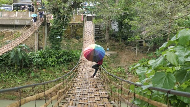 Man with a colorful umbrella standing on a hanging bridge in Asia