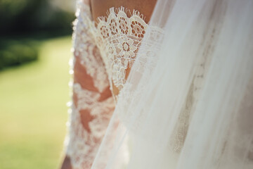 Beautiful white lace detail on back of bride's wedding gown. Outdoor background. Wedding day...