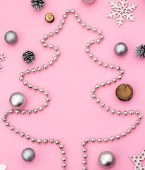 Christmas and New Year. Silhouette of a Christmas tree made of beads with Christmas toys and cones on a pink background. Flat lay. Copy space.