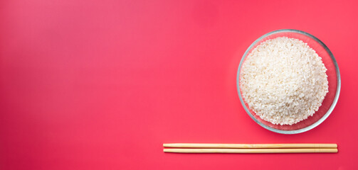 Flat lay. Transparent glass bowl with rice and chopsticks on a pink background. Traditional ingredients and symbols of Asian cuisine. The concept of food minimalism. Copy space. Banner.