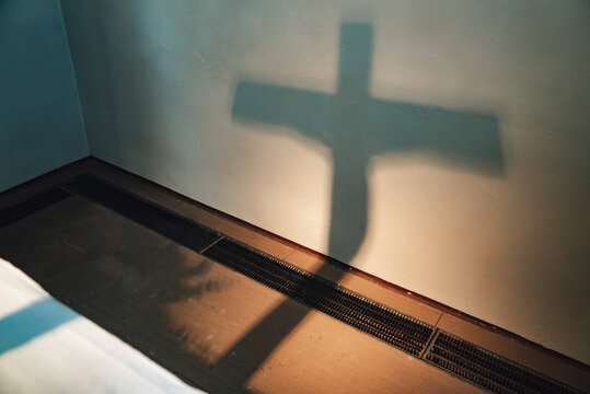 Shadow silhouette of Jesus Christ on the cross projected on wall. Play of light and shadows. Faith, Christianity and religion concept.
