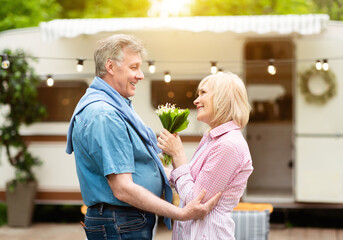 Celebrating anniversary. Mature woman holding flowers given by her caring husband on camping site