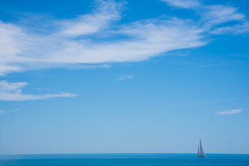 Calm sea with sailboat on the horizon. Blue sky seascape with copy space.