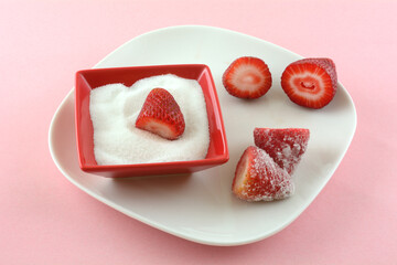 Fresh raw cut strawberries and sugar in red sugar bowl on white plate on pink background