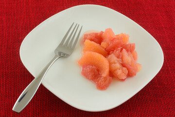 Red grapefruit and orange fruit cocktail serving on white plate with fork 