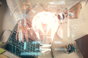 Double exposure of man's hands typing over computer keyboard and bulb hologram drawing. Top view....