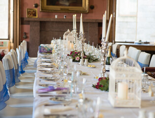 Long banquet table setting for home or party with candles, silverware and birdcage candle holders