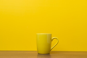 Yellow coffee cup on yellow background with copy space.
