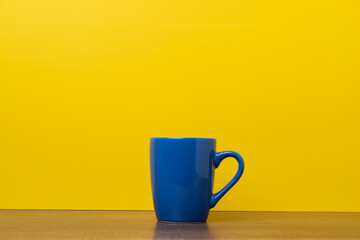 Blue coffee cup on yellow background with copy space.