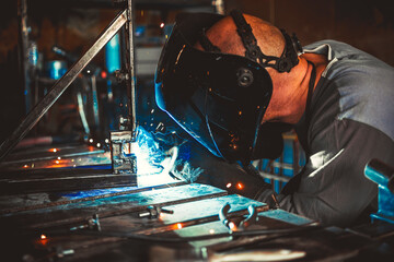 Fototapeta na wymiar Welder working in the workshop. Welding a metal construction. Sparkles and combustion. Hard work.