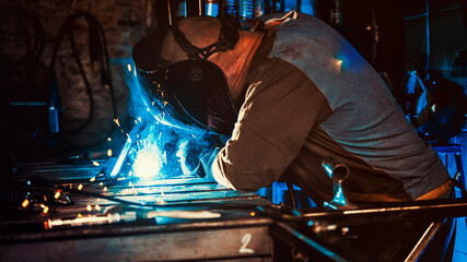 Welder working in the workshop. Welding a metal construction. Sparkles and combustion. Hard work.