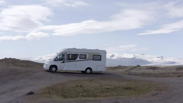 Aerial shot of caravan near snowcapped mountain against sky, drone flying forward over camper van - Southwestern Iceland, Iceland