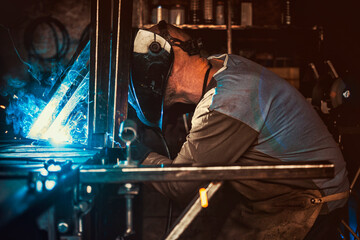 Welder working in the workshop. Welding a metal construction. Sparkles and combustion. Hard work.