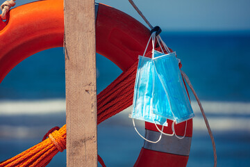 Fototapeta premium Conceptual scenery of masks near a lifebuoy ring in the beach. Preserve and stay safe by Coronavirus Covid19