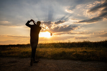 Jugador de golf  jugando al golf al atardecer, con el sol de frente y nubes en el cielo