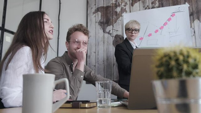 A woman is making a presentation of an idea at the chart board. The coworkers are discussing the project together and listening to the collegue.