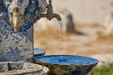 Ancient drinking fountain covered with moss. Water drops from a drinking fountain.
