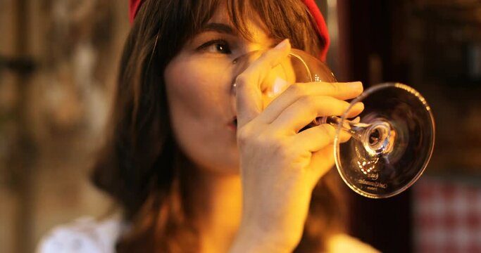 Close up portrait of pretty happy girl in red beret drinking red wine and smiling to camera while standing outdoors. Beautiful joyful female with glass of wine with smile on face. Rest concept