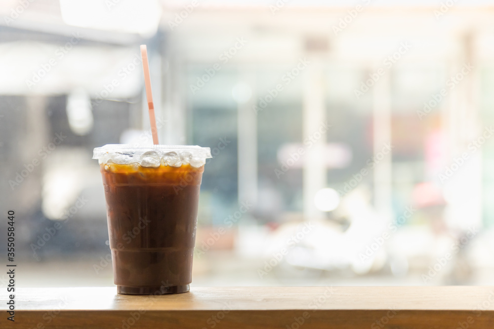 Wall mural Close up of take away plastic cup of iced black coffee (Americano) in restaurant on wooden table with copy sapce.