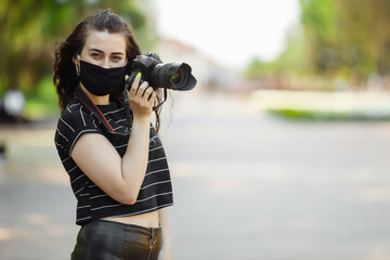 beautiful girl with a camera wears a medical mask and takes pictures in the park. Coronavirus 2019 nCoV pneumonia outbreak