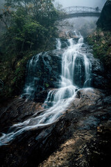 Silver waterfall in vietnam with arch bridge on a foggy day