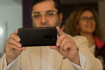 Man taking a picture with his cell phone and a woman on the background
