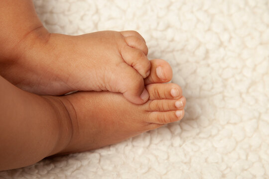 Baby's feet touching each other with toes curled. Baby has brown skin