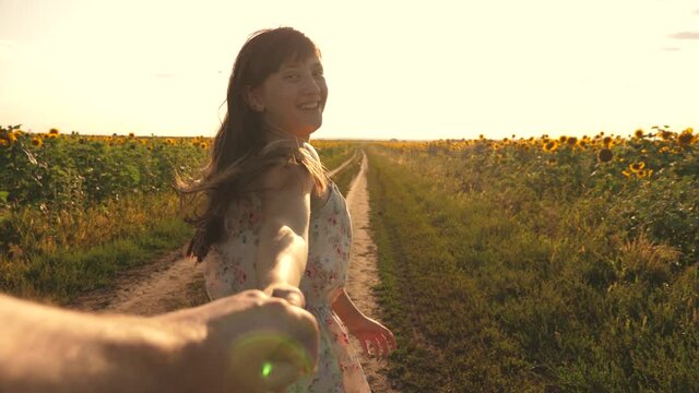 young girl travels in countryside with her boyfriend, they run across field of blooming sunflower. girl and guy rkuka in hand, in evening walk along field with sunflowers at sunset, holding hands.