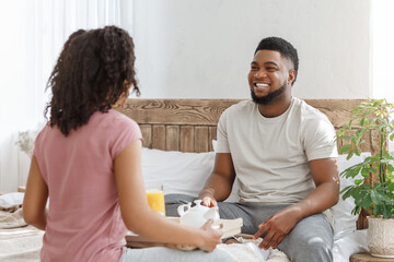 Cheerful black man looking at his girlfriend, breakfast in bed