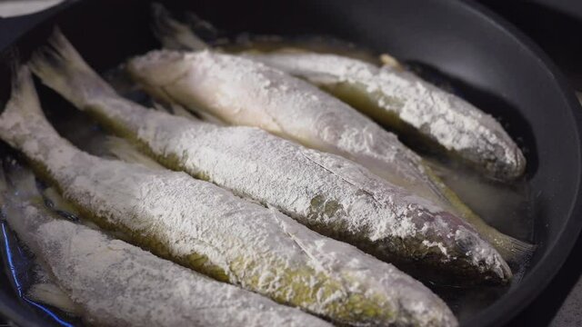 Large smelt is fried in oil in a black pan. Fish sprinkled with flour.