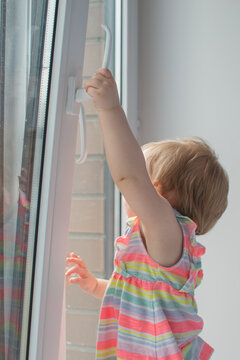 Little Girl Opens The Window. Children Safety At Home. Prevention Of Falling Accident