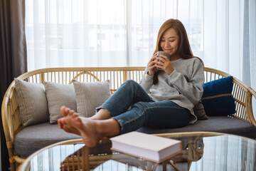 A beautiful asian woman drinking hot coffee while sitting on a sofa at home in the morning