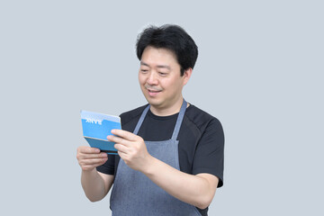A middle-aged Asian man holding a bank passbook in his hand on a gray background.