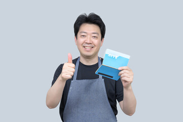 A middle-aged Asian man holding a bank passbook in his hand on a gray background.