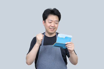 A middle-aged Asian man holding a bank passbook in his hand on a gray background.