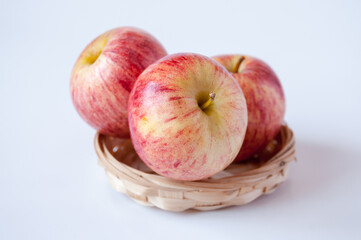 Three red apples in a wicker plate on a white background