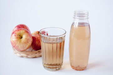 Three red apples in a wicker plate, a glass and a bottle of Apple juice on a white background
