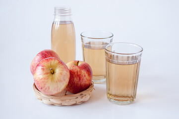 Three red apples in a wicker plate, a glass and a bottle of Apple juice on a white background