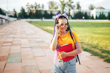 Young beautiful girl holding a red folder in her hand in a yellow T-shirt walking in the open air at a sports stadium