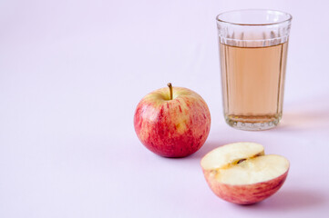 A glass of Apple juice and a whole and half red Apple on a pink background