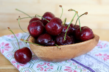 Ripe red cherries in a wooden plate with a brown towel on a wooden background
