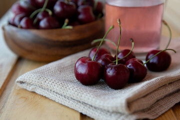 Ripe red cherries in a wooden plate with a glass of juice  and a brown towel on a wooden background