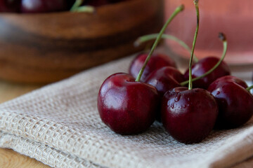 Ripe red cherries in a wooden plate with a glass of juice  and a brown towel on a wooden background