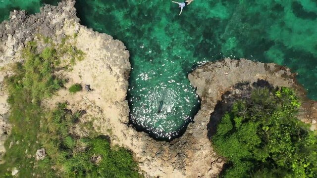 A young caucasian woman is swimming on the surface in a bikini, wearing big blue fins to snorkel and explore the fish and corals beneath her. Dancing reflections from the sun in the colorful water.