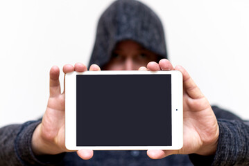 Young caucasian man in dark gray sweatshirt with hood holds tablet pc computer with blank screen for copy space isolated on white background. Concept of technology