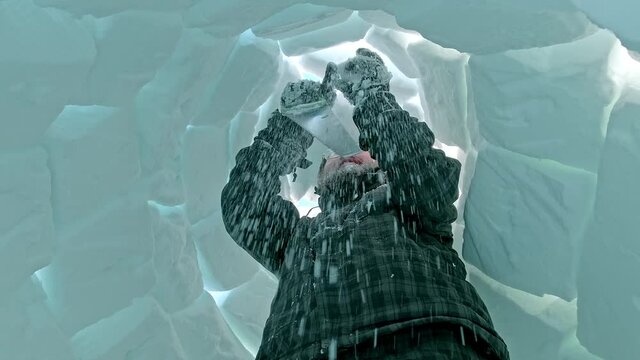 bearded tourist fixes white snow blocks on igloo top with metal saw standing inside construction close low angle shot