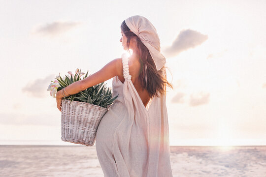 beautiful young stylish woman with basket with flowers outdoors at sunset